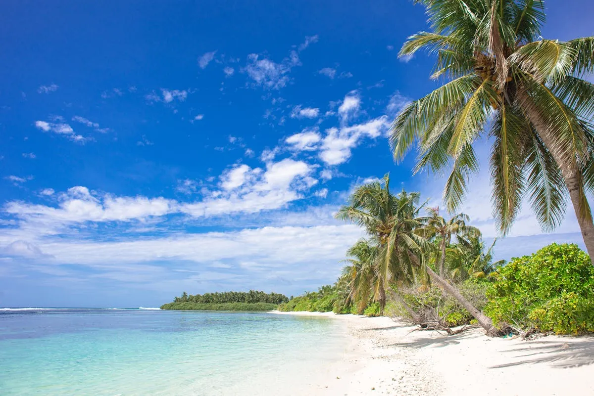 A Maldivian beach with white sand under blue skies and clouds